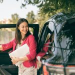 Young confident woman getting out of the car with her laptop and going to work.